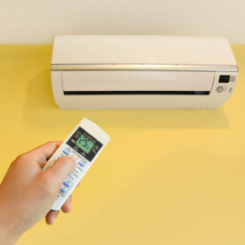 Hand turning on home air conditioning system at 25 degree, energy saving modern air con In London UK